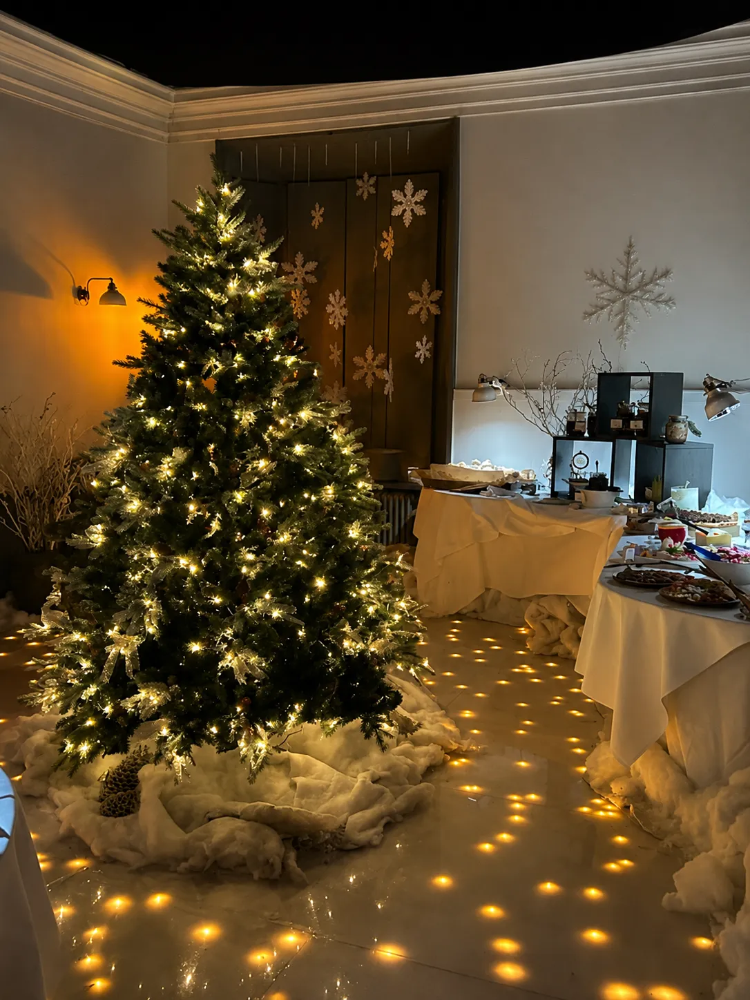 Upplyst julgran med snö och snöflingor intill dukade dessertbord i slottets sal