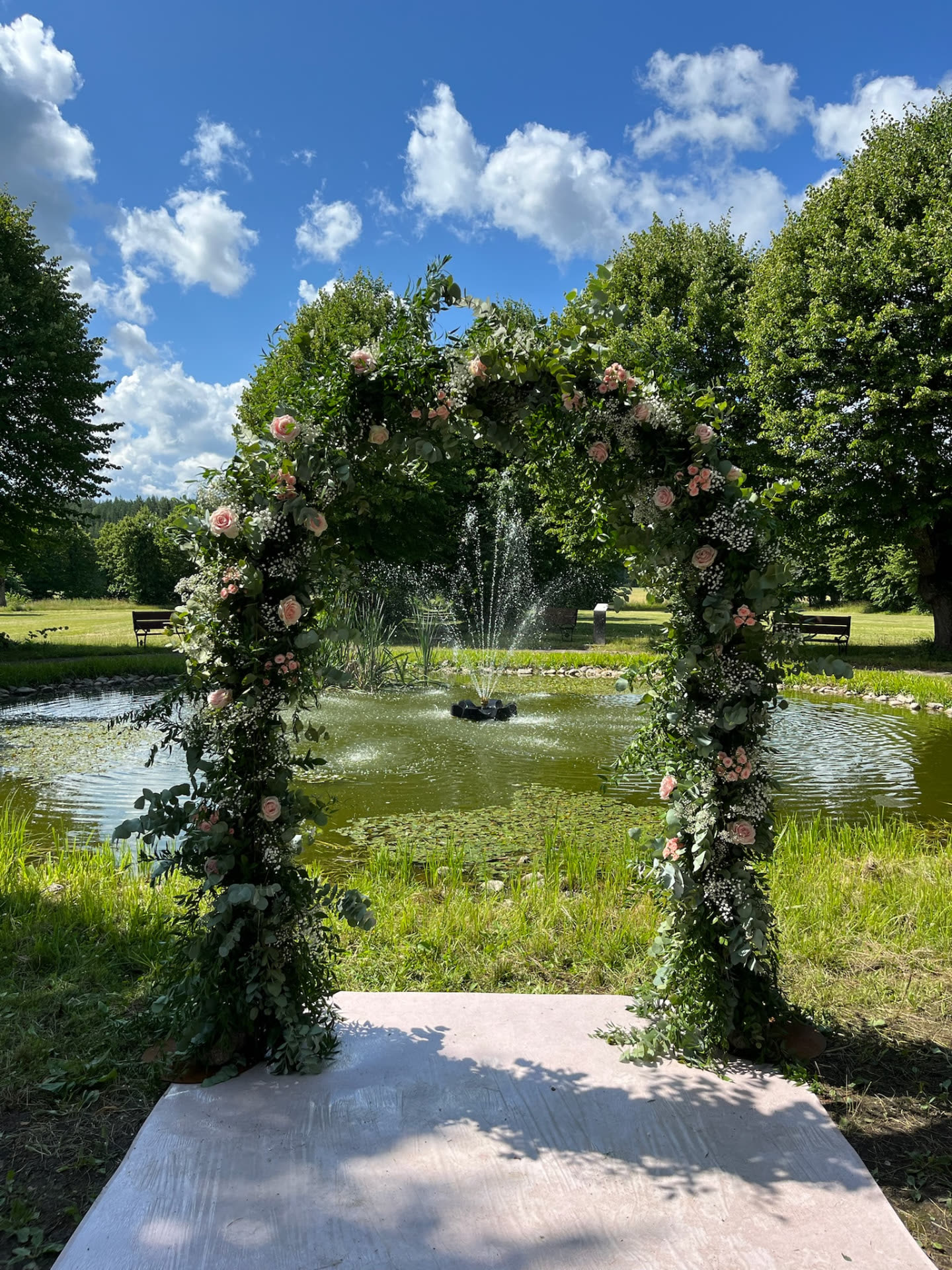 Blomsterbåge med rosor och eukalyptus framför fontänen
