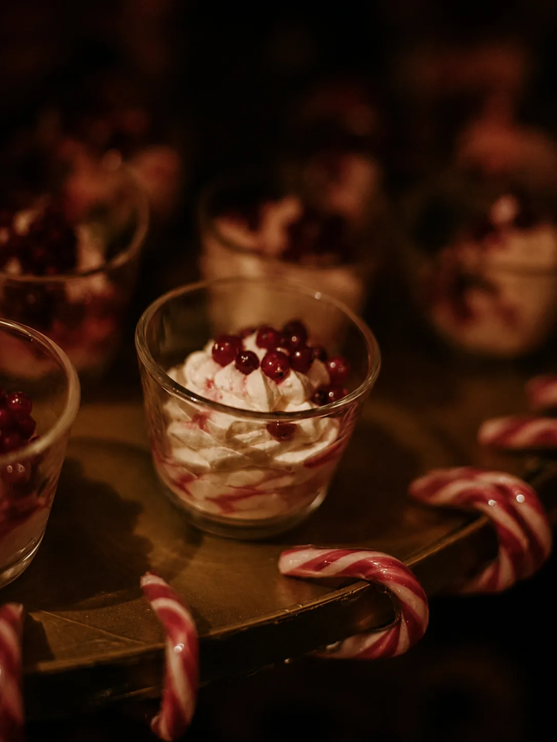 Juldessert med vispad grädde och lingon i glas bredvid polkagrisar