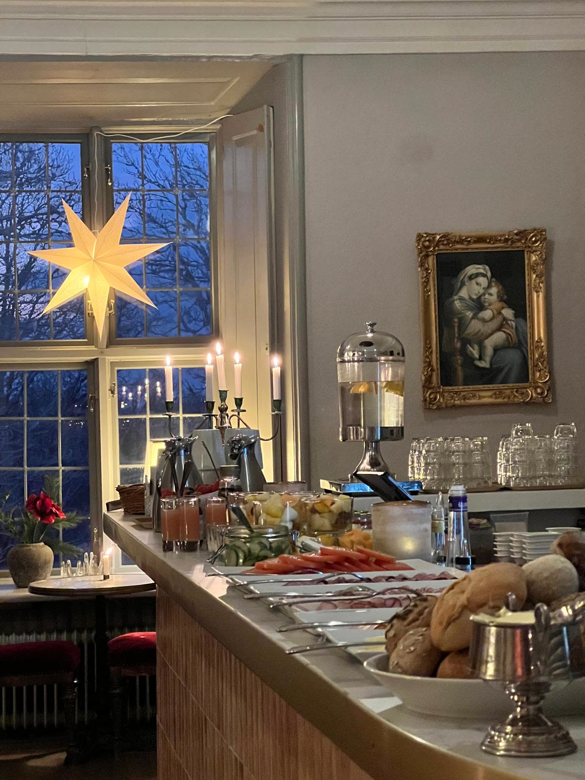Frukostbuffé med bröd, chark och adventsstjärna i vinterblått fönsterljus