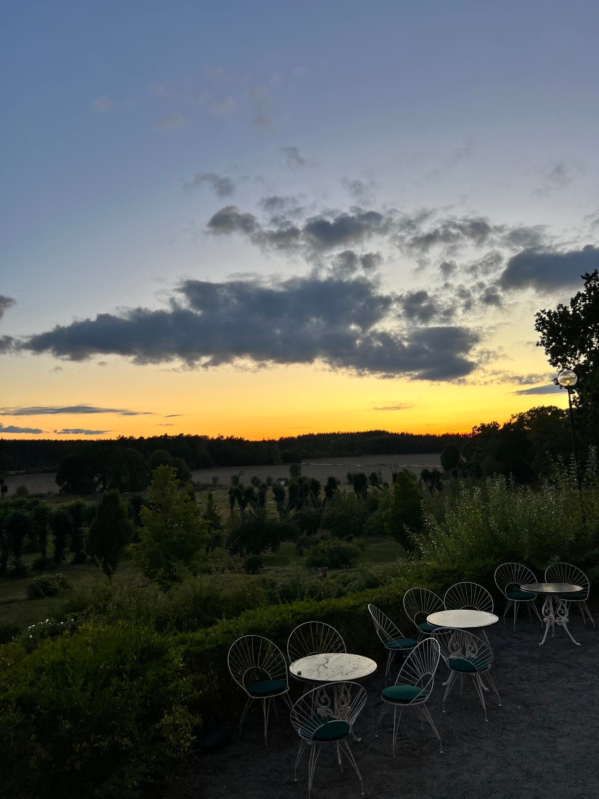 Terrassens caféstolar mot solnedgången över parken och fälten